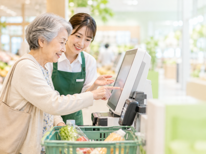 セルフレジの操作を店員に確認するシニア女性のイメージ